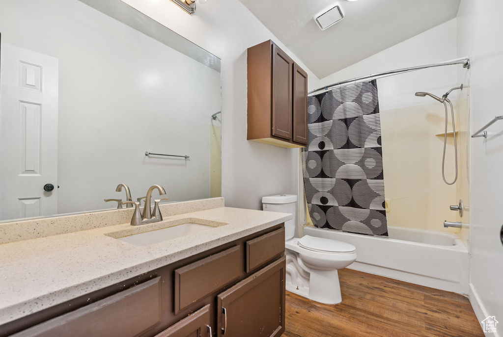 Full bath featuring toilet, vanity, shower / tub combo, wood finished floors, and vaulted ceiling