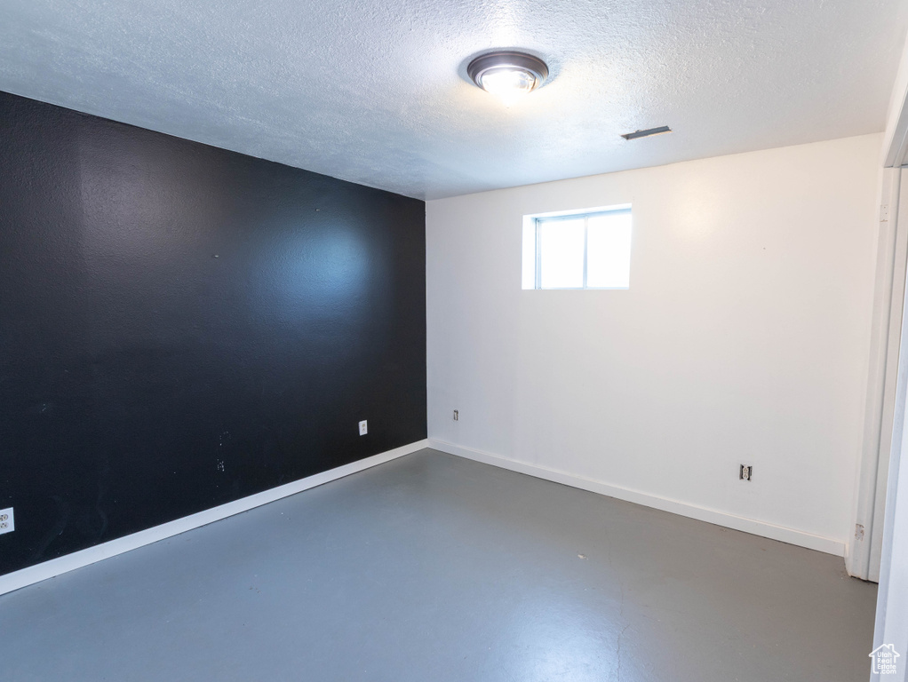 Spare room with finished concrete flooring, a textured ceiling, and baseboards
