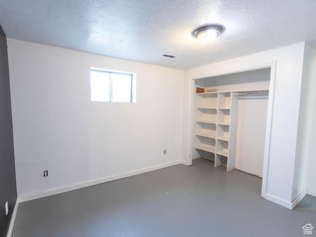 Unfurnished bedroom featuring a textured ceiling, finished concrete flooring, baseboards, and a closet