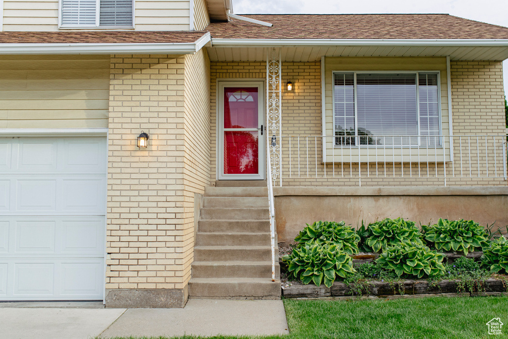 Property entrance with brick siding, roof with shingles, a porch, and an attached garage