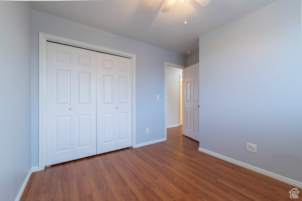 Unfurnished bedroom featuring wood finished floors, baseboards, a closet, and a ceiling fan