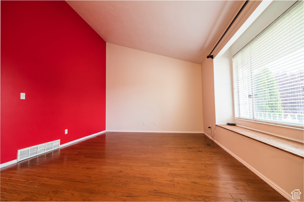 Unfurnished room featuring lofted ceiling, wood finished floors, and baseboards