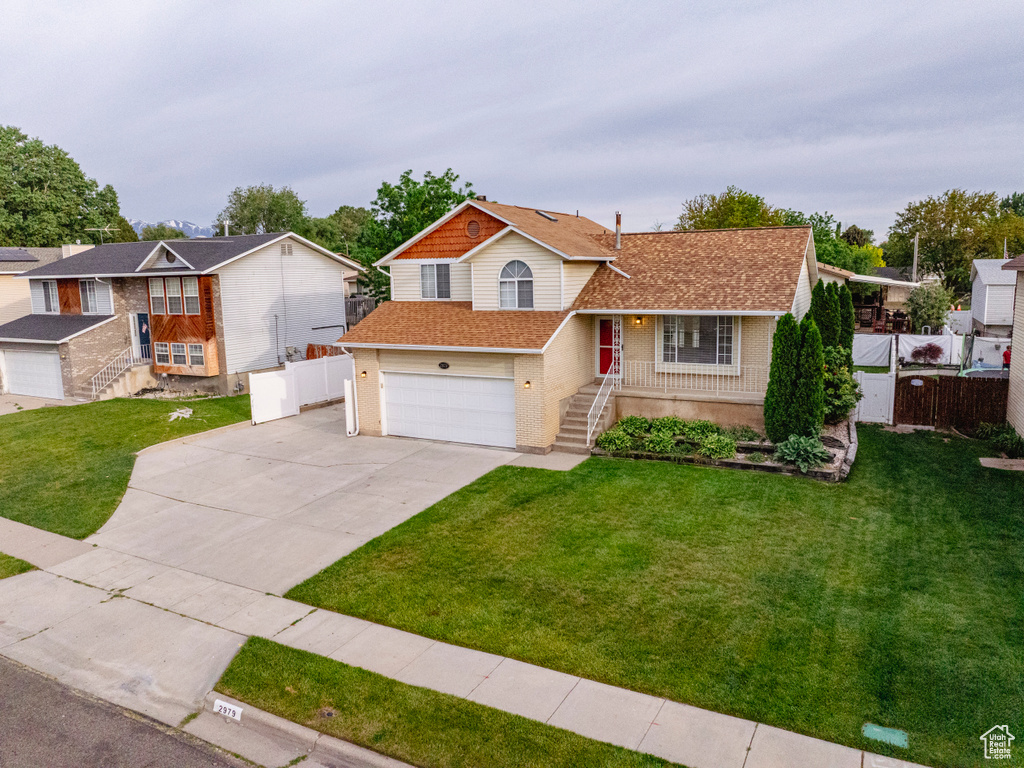 Tri-level home featuring concrete driveway, roof with shingles, an attached garage, brick siding, and stairway