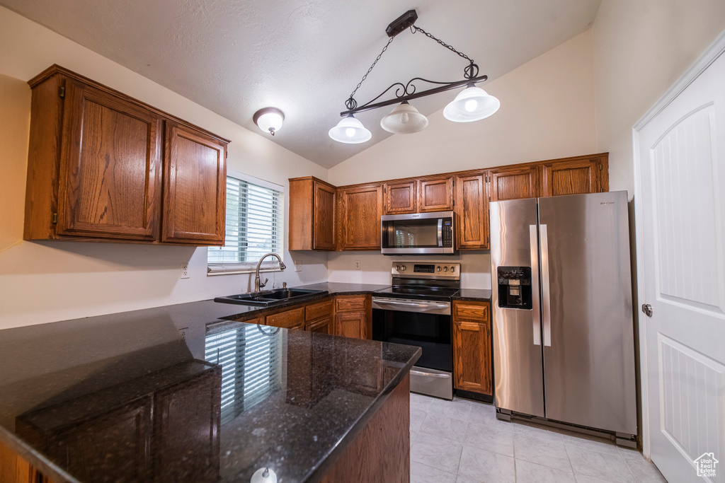 Kitchen featuring stainless steel appliances, lofted ceiling, a sink, dark stone countertops, and light tile patterned floors