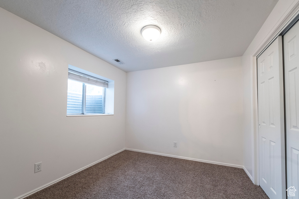 Unfurnished bedroom featuring a textured ceiling, carpet floors, a closet, and baseboards