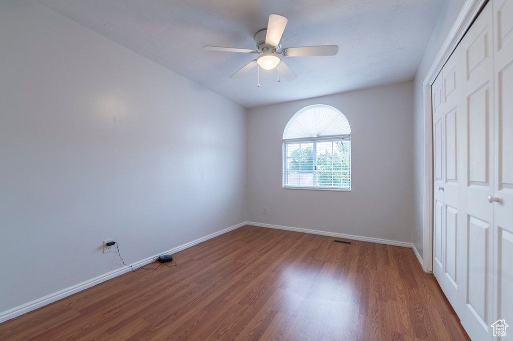 Unfurnished bedroom featuring a closet, wood finished floors, baseboards, and ceiling fan