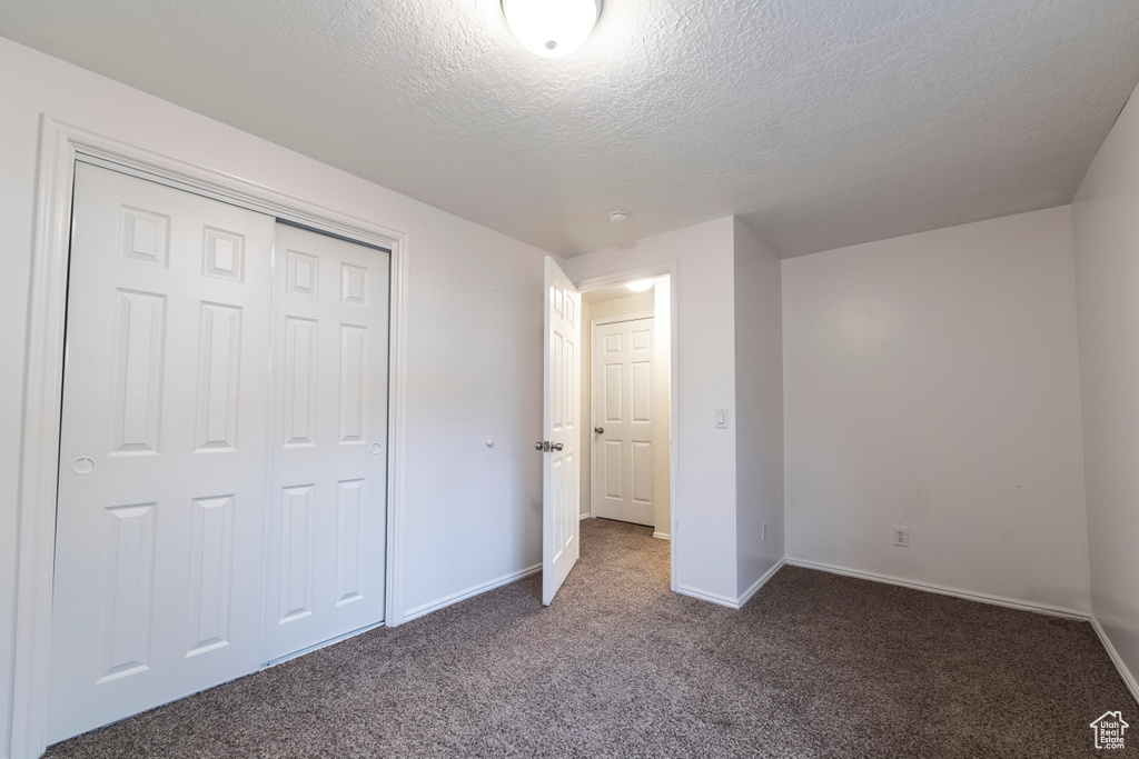 Unfurnished bedroom featuring a textured ceiling, carpet, baseboards, and a closet