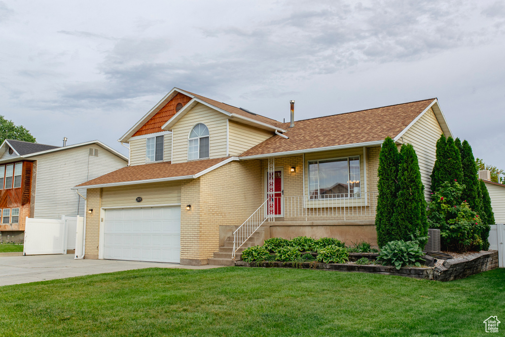 Split level home featuring concrete driveway, a garage, a shingled roof, and brick siding