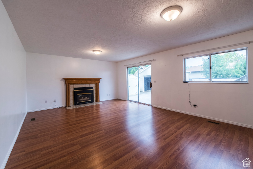 Unfurnished living room featuring a fireplace, a textured ceiling, wood finished floors, and baseboards
