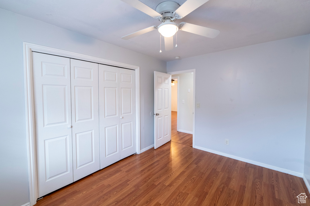 Unfurnished bedroom featuring wood finished floors, baseboards, a closet, and a ceiling fan