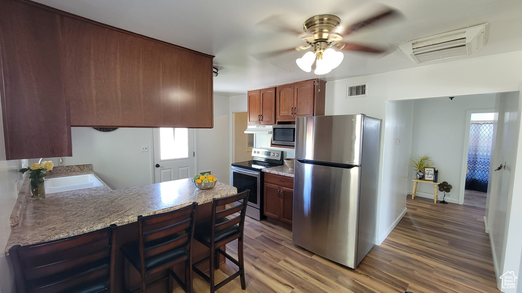 Kitchen featuring stainless steel appliances, a sink, wood finished floors, a ceiling fan, and a peninsula