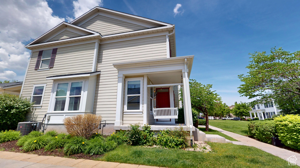 View of front of home with central AC unit, covered porch, and a front yard