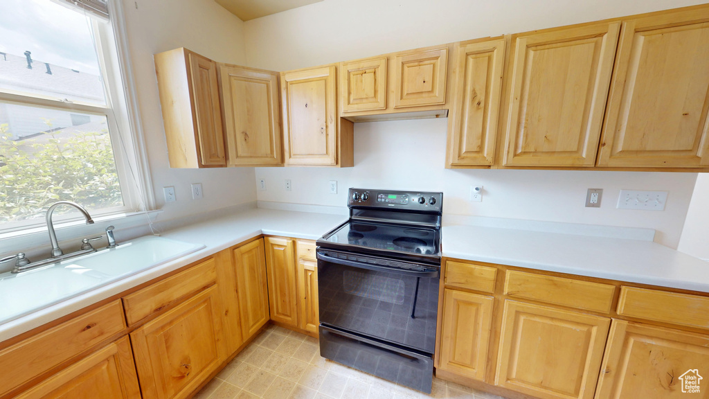 Kitchen featuring black electric range oven, light brown cabinets, light countertops, and a sink