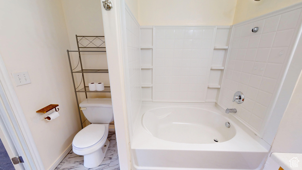 Full bathroom featuring toilet, marble look tiles, baseboards, and bathtub / shower combination