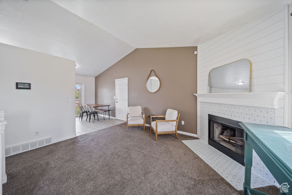 Living area with a tile fireplace, carpet flooring, vaulted ceiling, and baseboards