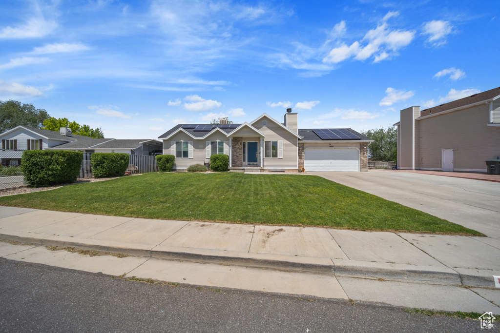 Ranch-style home with driveway, solar panels, an attached garage, and a chimney