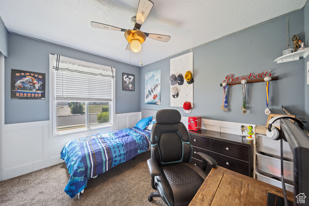 Bedroom featuring carpet flooring, wainscoting, a desk, a textured ceiling, and ceiling fan