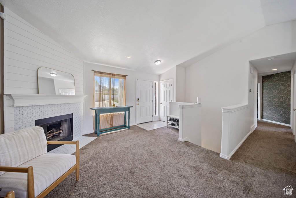 Carpeted living room with vaulted ceiling, a tile fireplace, and baseboards