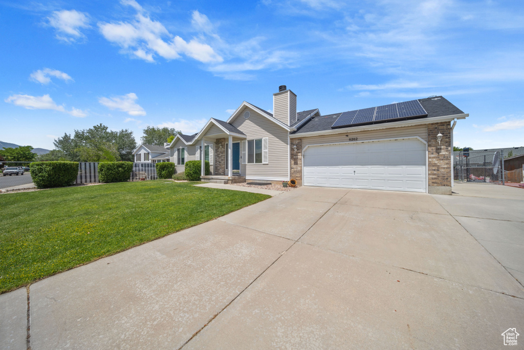 View of front of property featuring concrete driveway, solar panels, an attached garage, and a chimney