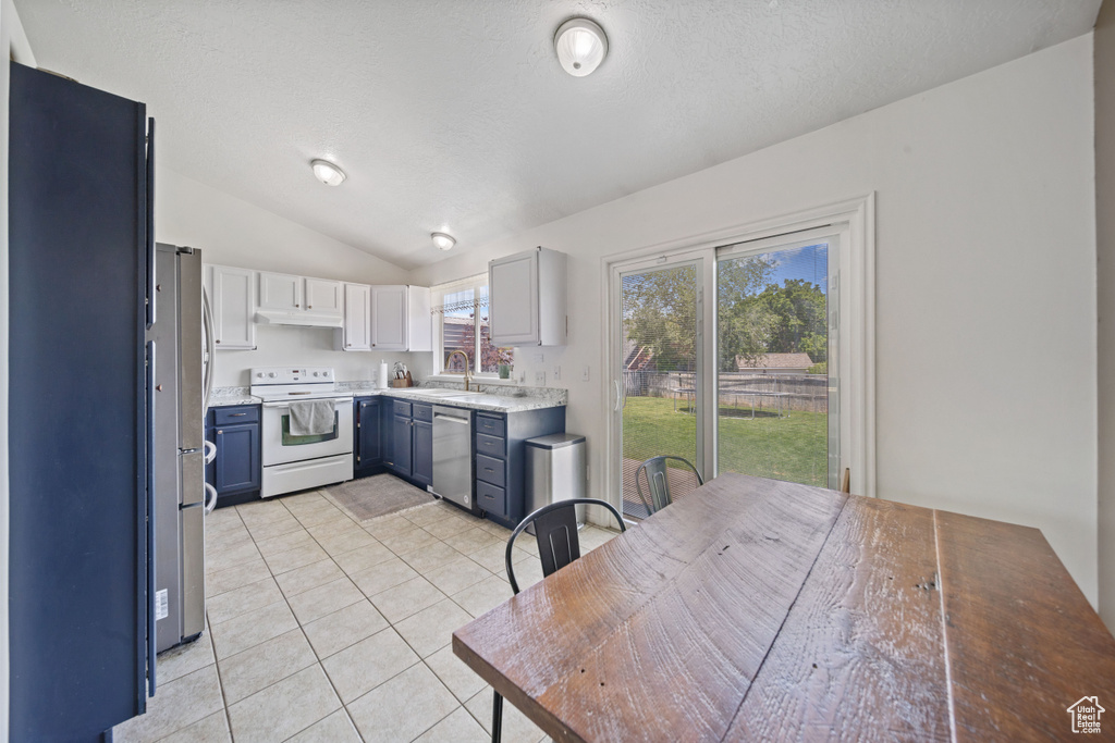 Kitchen with stainless steel appliances, blue cabinets, lofted ceiling, light countertops, and light tile patterned floors