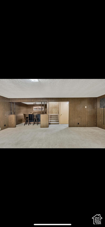 Finished basement with a textured ceiling, carpet flooring, wooden walls, and stairs