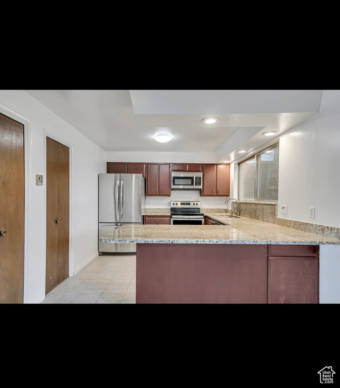 Kitchen with appliances with stainless steel finishes, a sink, a peninsula, light tile patterned floors, and light stone countertops