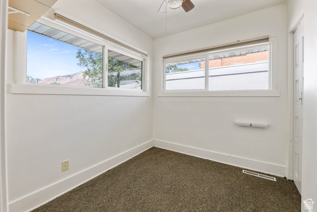Empty room featuring dark colored carpet, baseboards, and a ceiling fan