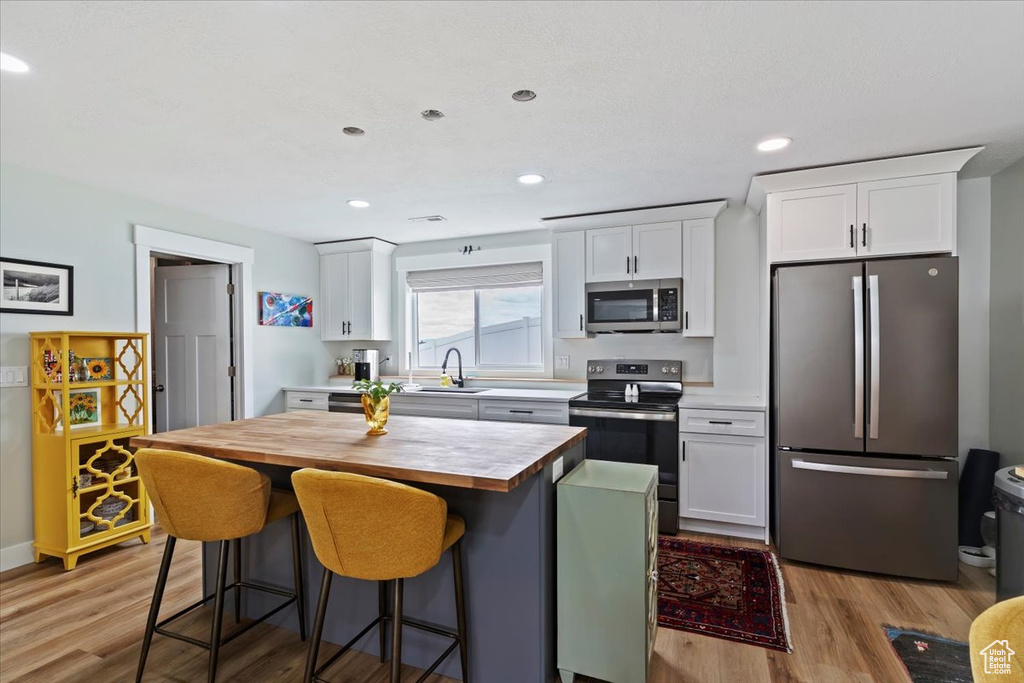 Kitchen with appliances with stainless steel finishes, a sink, butcher block counters, light wood-type flooring, and white cabinets