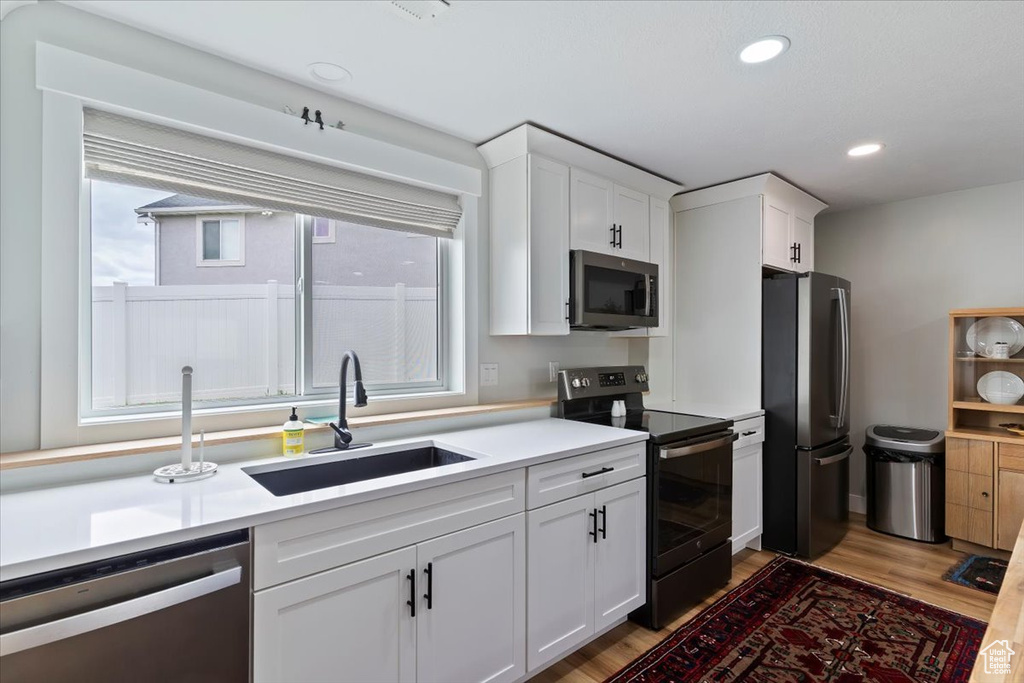 Kitchen with appliances with stainless steel finishes, a sink, light wood finished floors, white cabinetry, and recessed lighting