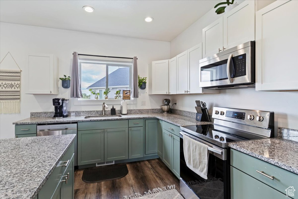 Kitchen with appliances with stainless steel finishes, a sink, dark wood finished floors, white cabinets, and recessed lighting