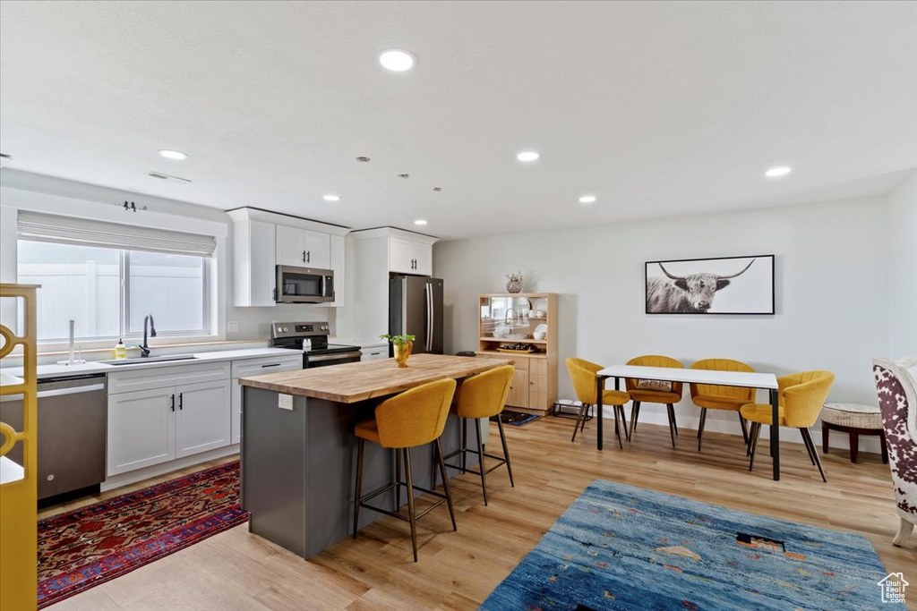 Kitchen featuring appliances with stainless steel finishes, a sink, wooden counters, a kitchen bar, and white cabinets