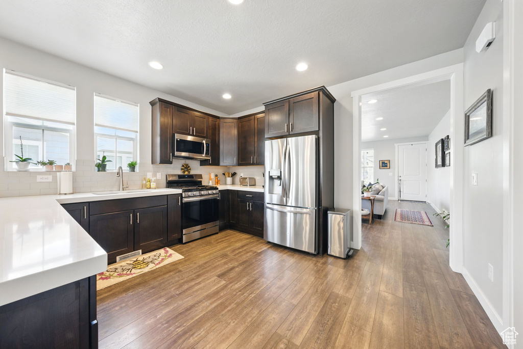 Kitchen with appliances with stainless steel finishes, a sink, light wood-style flooring, dark brown cabinets, and plenty of natural light