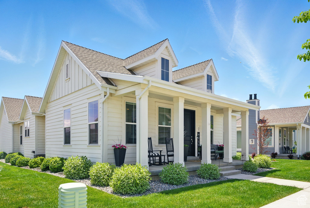 View of front of house featuring covered porch, board and batten siding, a front yard, and a shingled roof