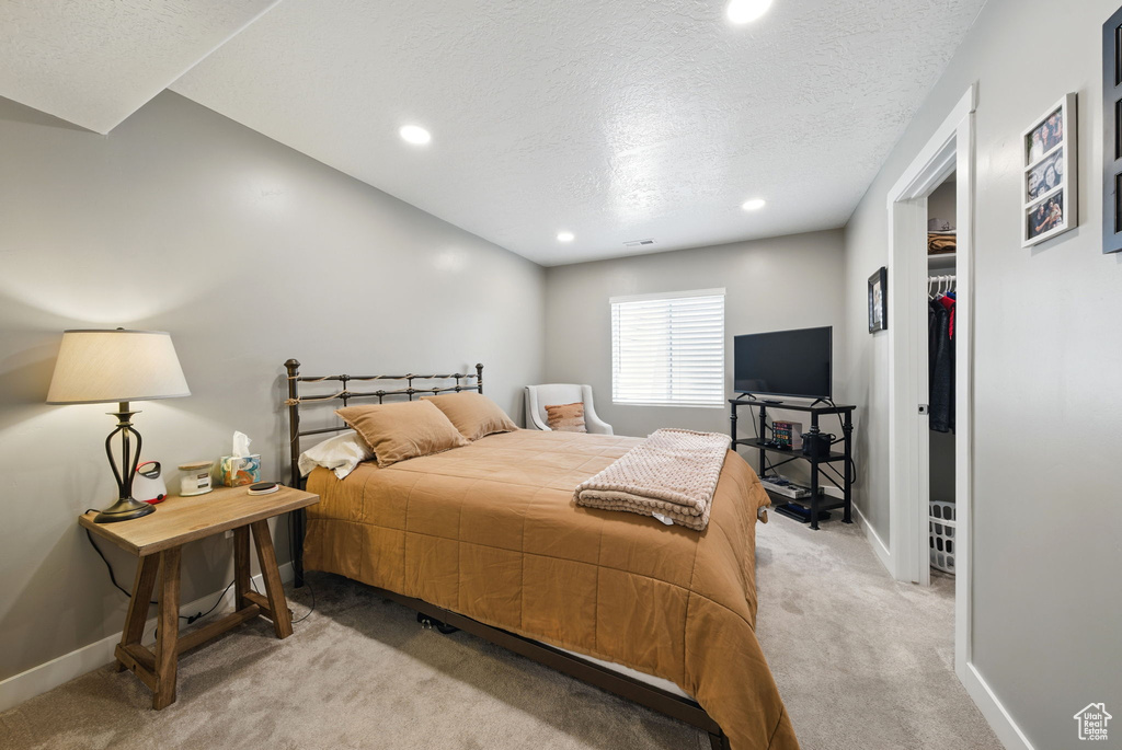 Bedroom featuring light carpet, baseboards, a walk in closet, a textured ceiling, and recessed lighting
