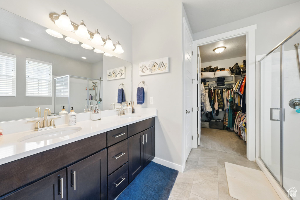 Full bath featuring a shower stall, a spacious closet, double vanity, and baseboards