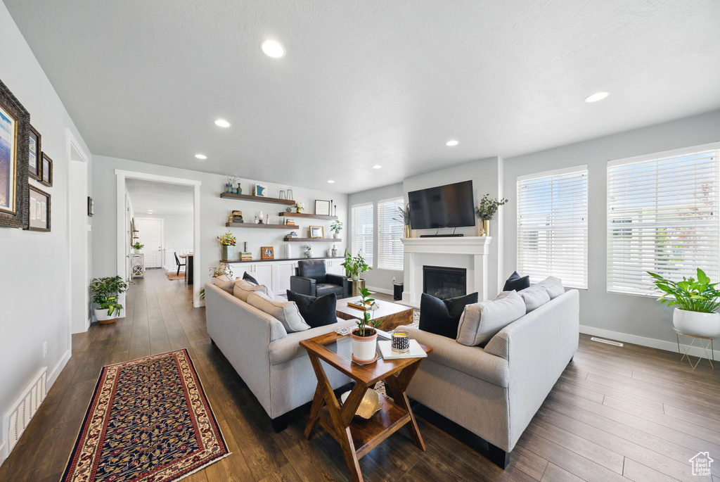 Living room with a fireplace, dark wood-style floors, recessed lighting, and baseboards