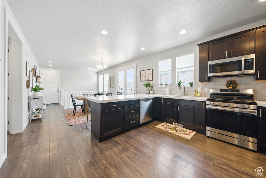 Kitchen with appliances with stainless steel finishes, a peninsula, light countertops, dark wood-style floors, and recessed lighting
