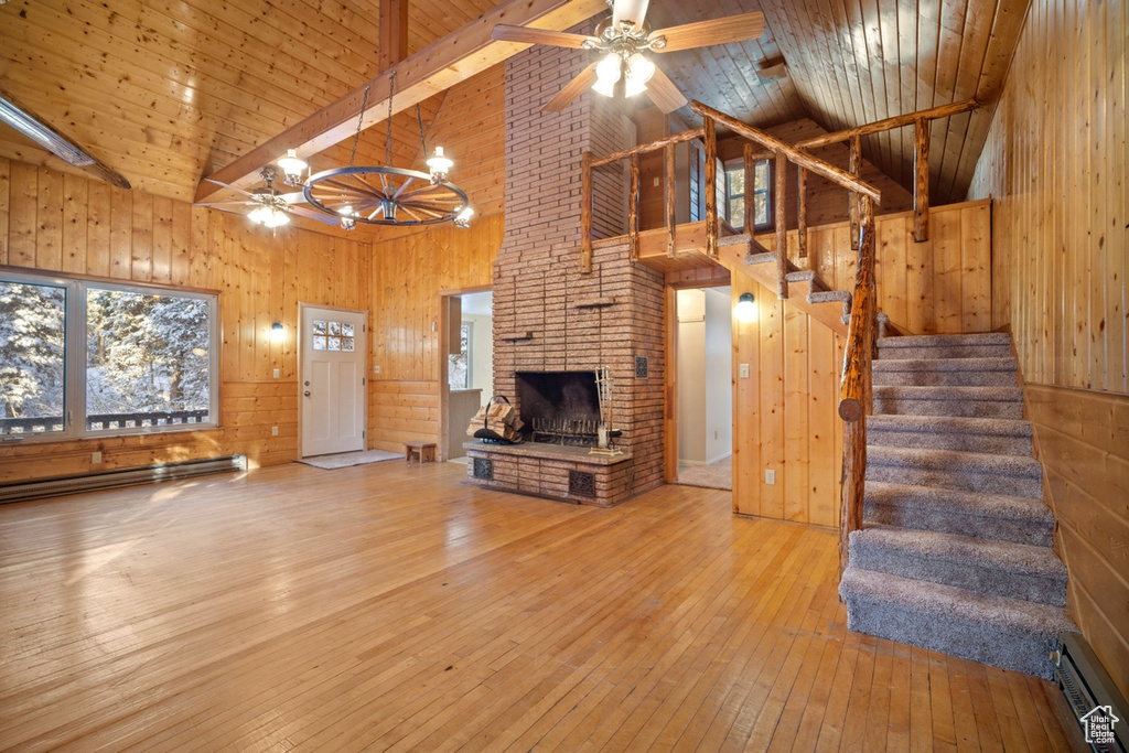 Unfurnished living room with ceiling fan, high vaulted ceiling, a baseboard radiator, wooden walls, and hardwood / wood-style flooring
