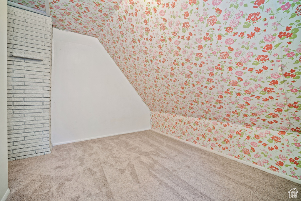 Carpeted spare room featuring wallpapered walls, lofted ceiling, and baseboards