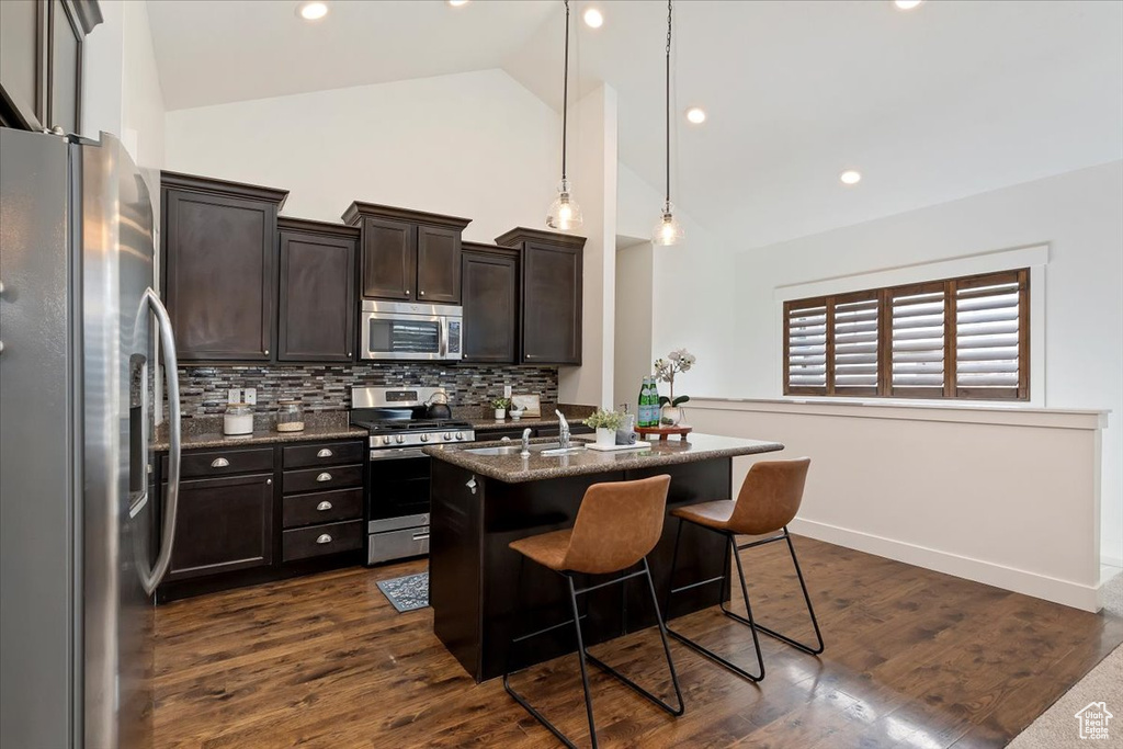 Kitchen with appliances with stainless steel finishes, decorative backsplash, a kitchen bar, high vaulted ceiling, and dark brown cabinetry
