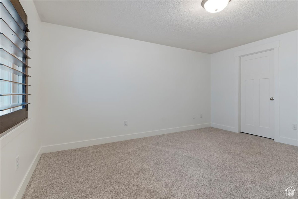 Unfurnished bedroom featuring light colored carpet, a textured ceiling, and baseboards