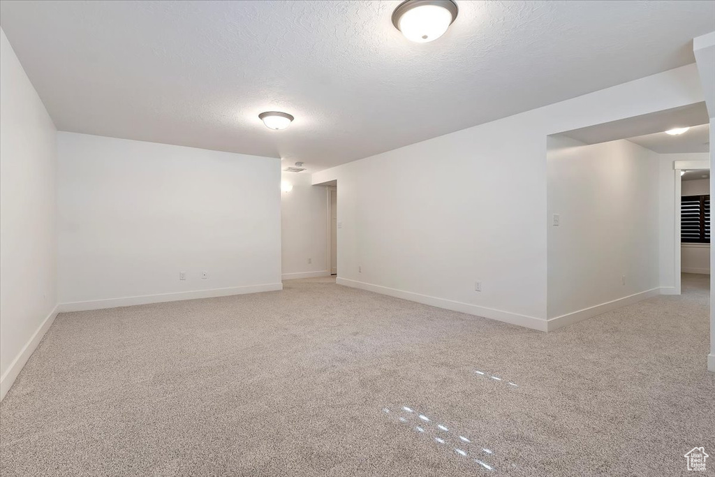 Spare room featuring light carpet, a textured ceiling, and baseboards