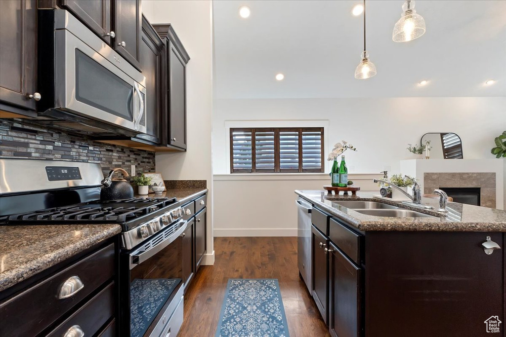 Kitchen featuring appliances with stainless steel finishes, a sink, an island with sink, backsplash, and dark stone counters
