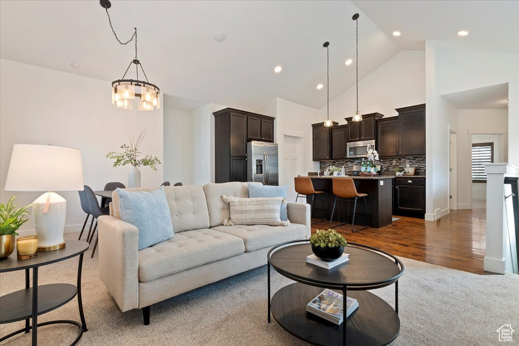 Living area featuring a chandelier, high vaulted ceiling, baseboards, recessed lighting, and wood finished floors
