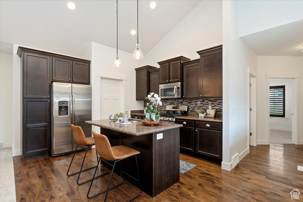 Kitchen with appliances with stainless steel finishes, dark brown cabinetry, a kitchen bar, tasteful backsplash, and a kitchen island with sink