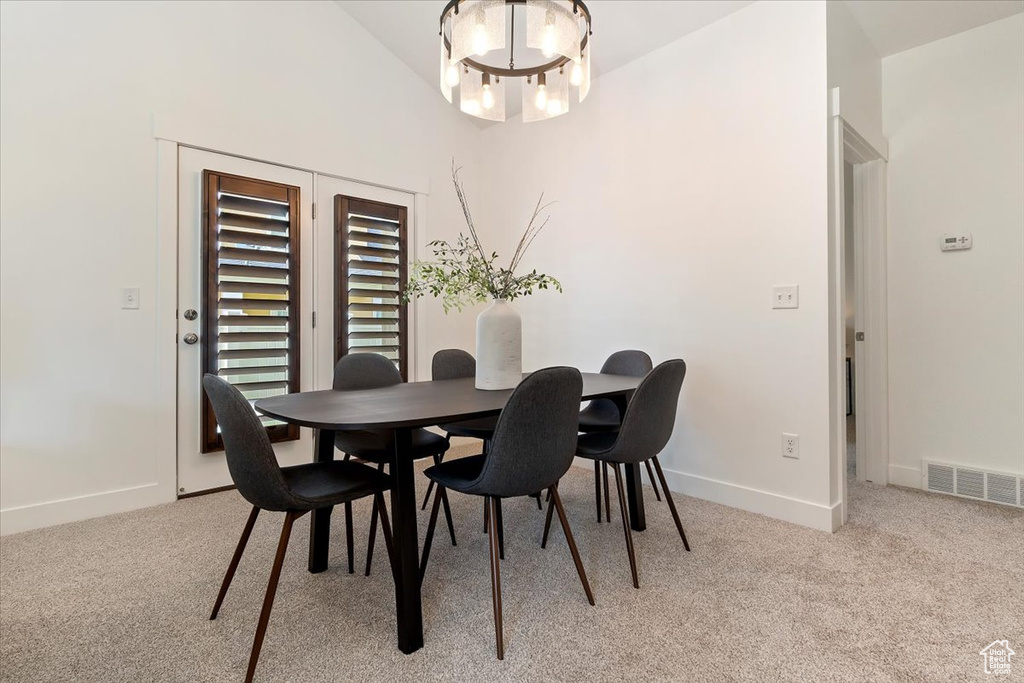 Dining area featuring a chandelier, light colored carpet, baseboards, and vaulted ceiling