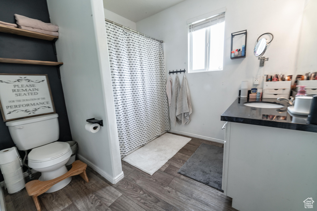 Bathroom with vanity, toilet, wood finished floors, baseboards, and curtained shower