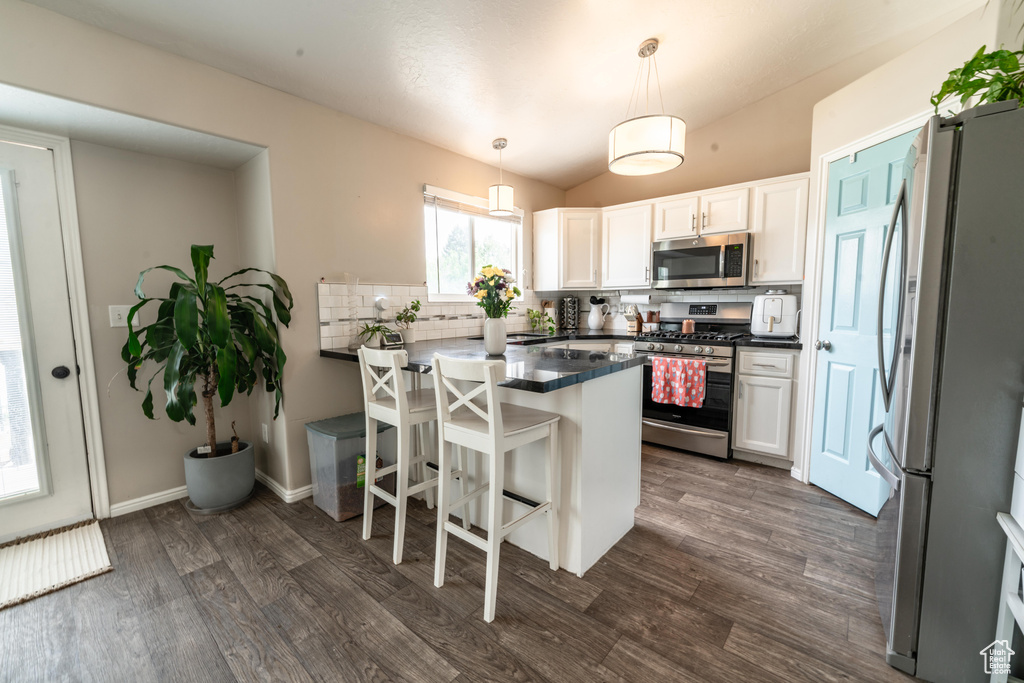 Kitchen with appliances with stainless steel finishes, a peninsula, dark countertops, backsplash, and dark wood-type flooring