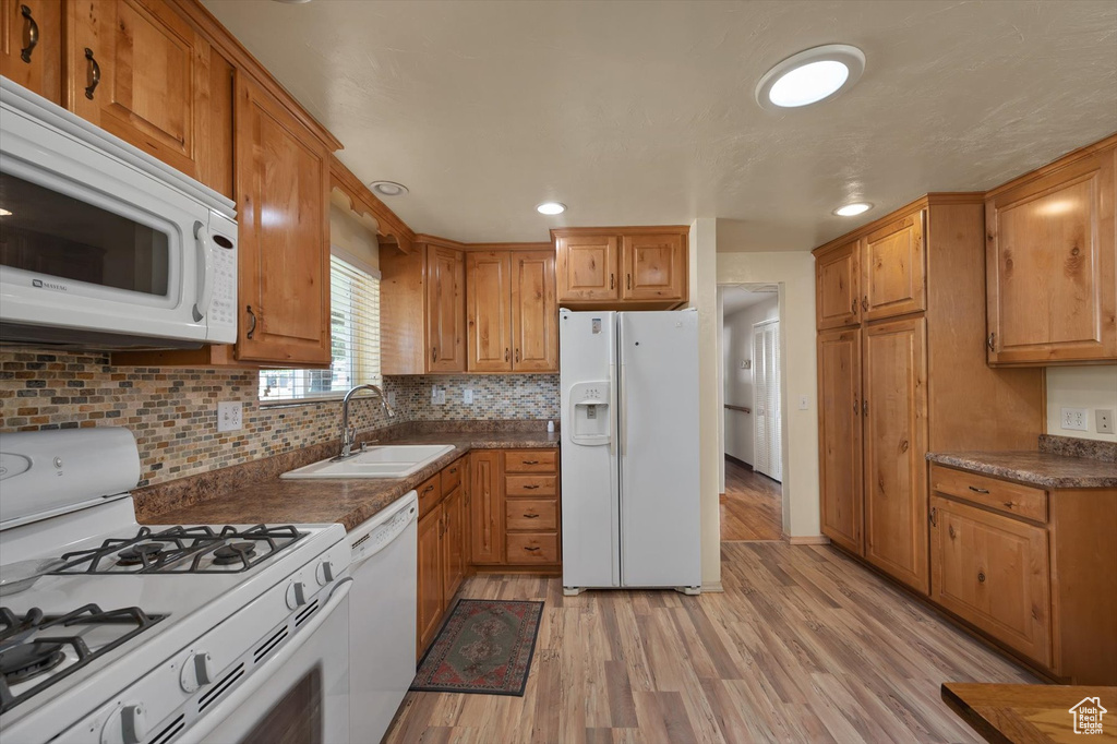 Kitchen with white appliances, a sink, light wood-style floors, brown cabinets, and recessed lighting