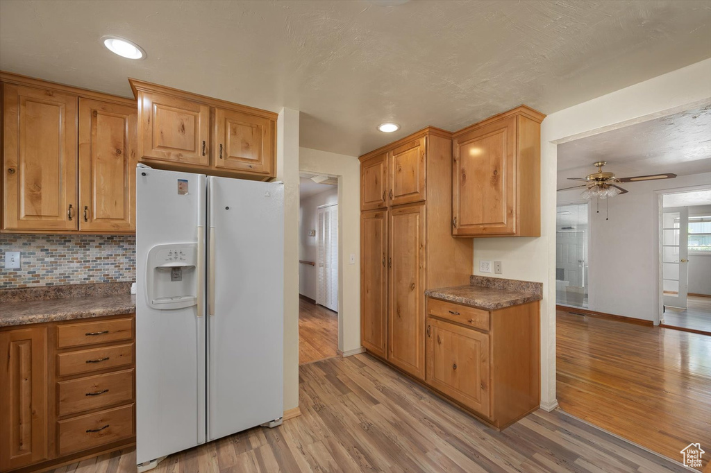 Kitchen with white refrigerator with ice dispenser, light wood-style flooring, a ceiling fan, baseboards, and dark countertops